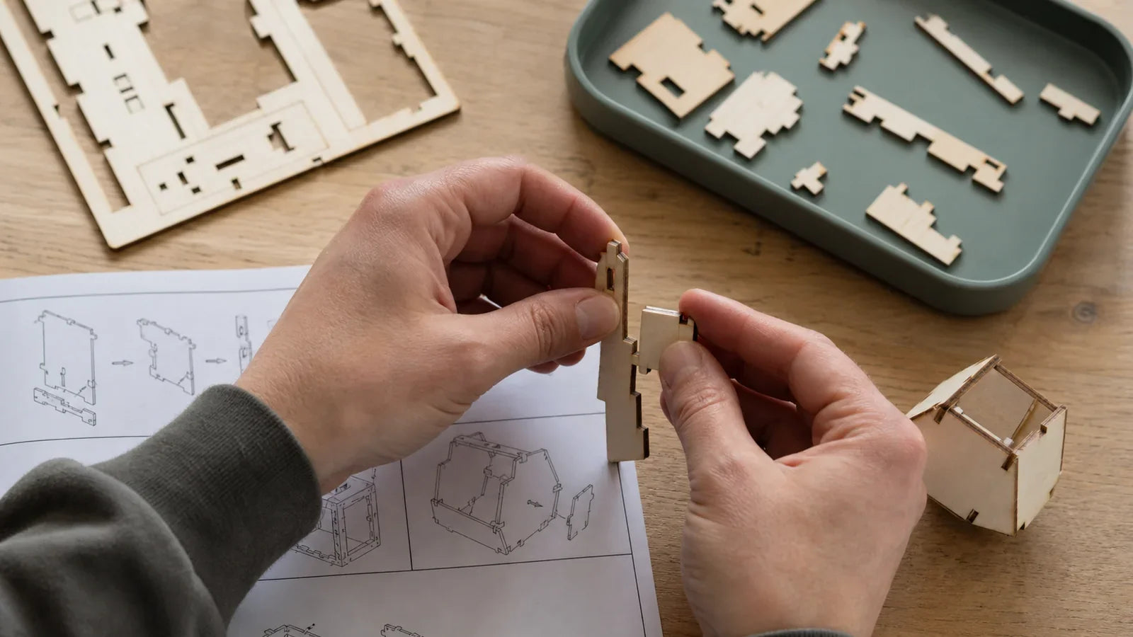 Hands fitting two simple wooden model pieces together beside organized parts